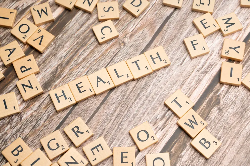 Scrabble game letters on a table spell out the word Health on a natural wood surface
